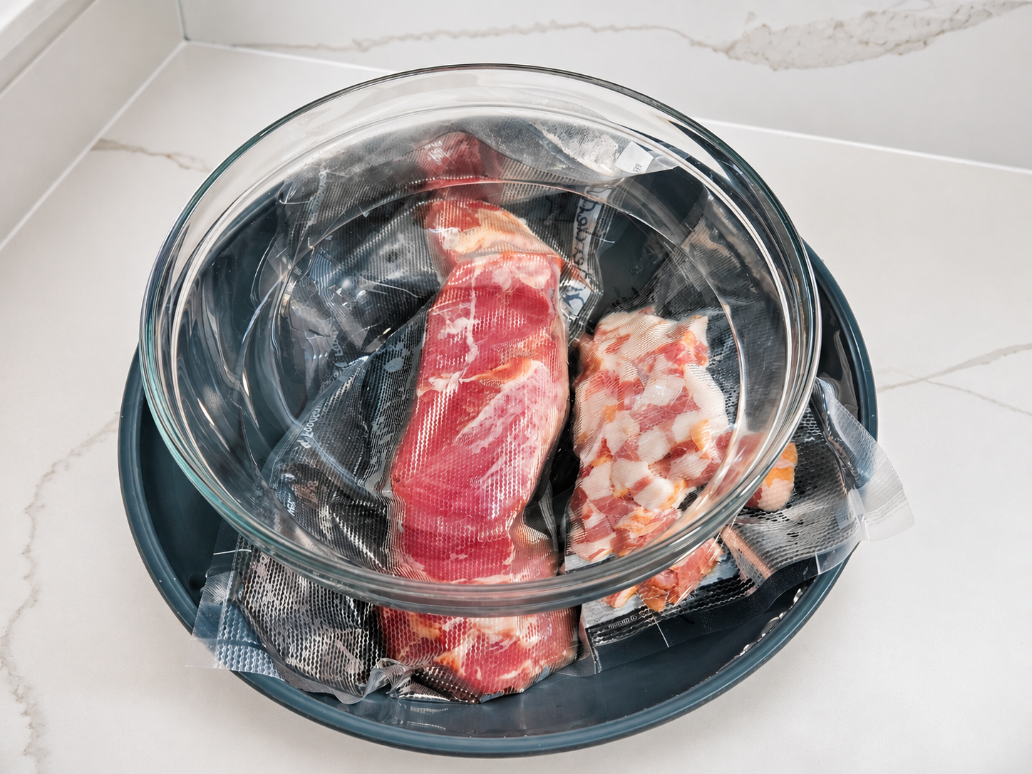 Vacuum-sealed raw meat portions placed inside a bowl, submerged in cold water, with a glass bowl on top for safe thawing.