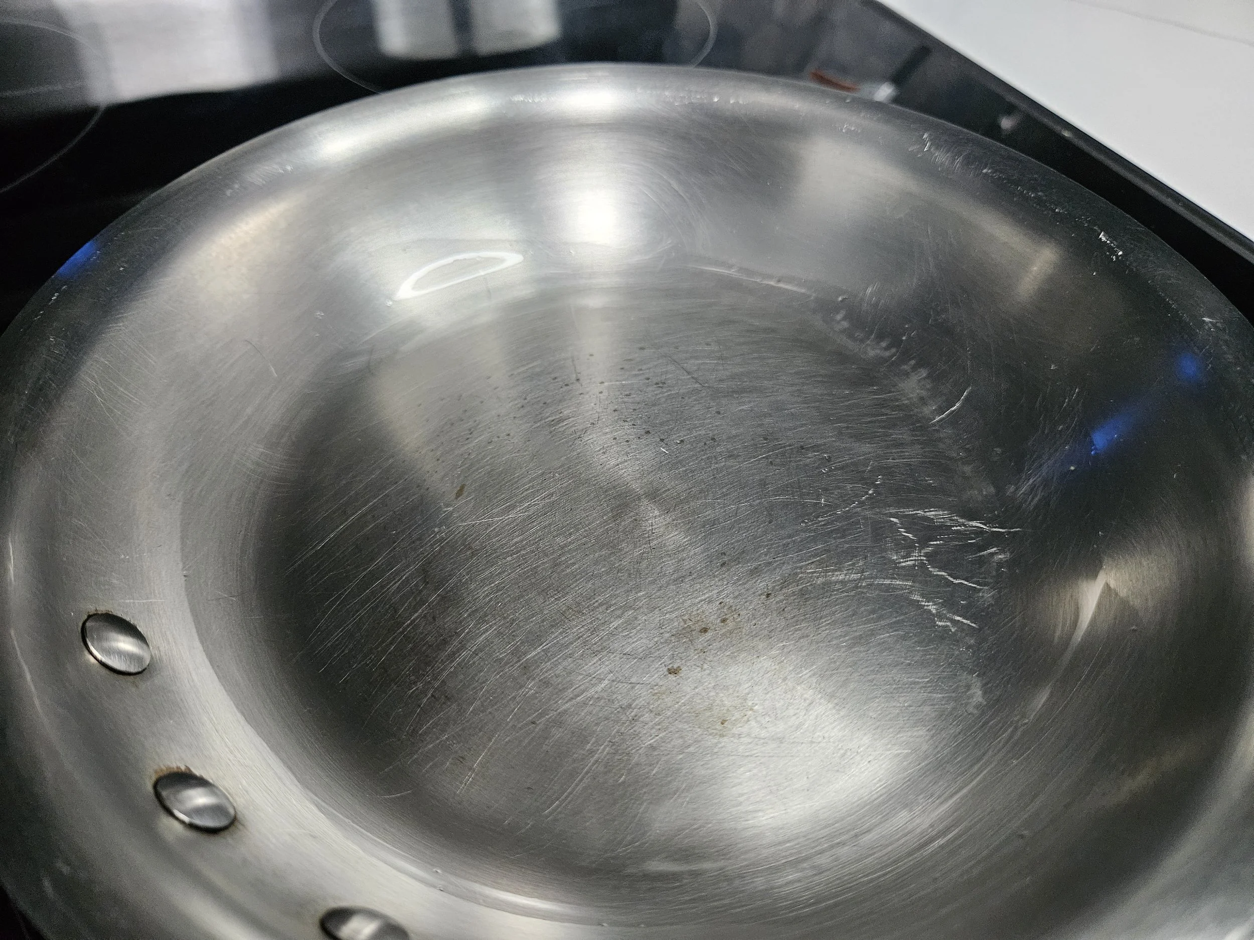 Stainless steel frying pan with overheated oil beginning to produce faint wisps of smoke.
