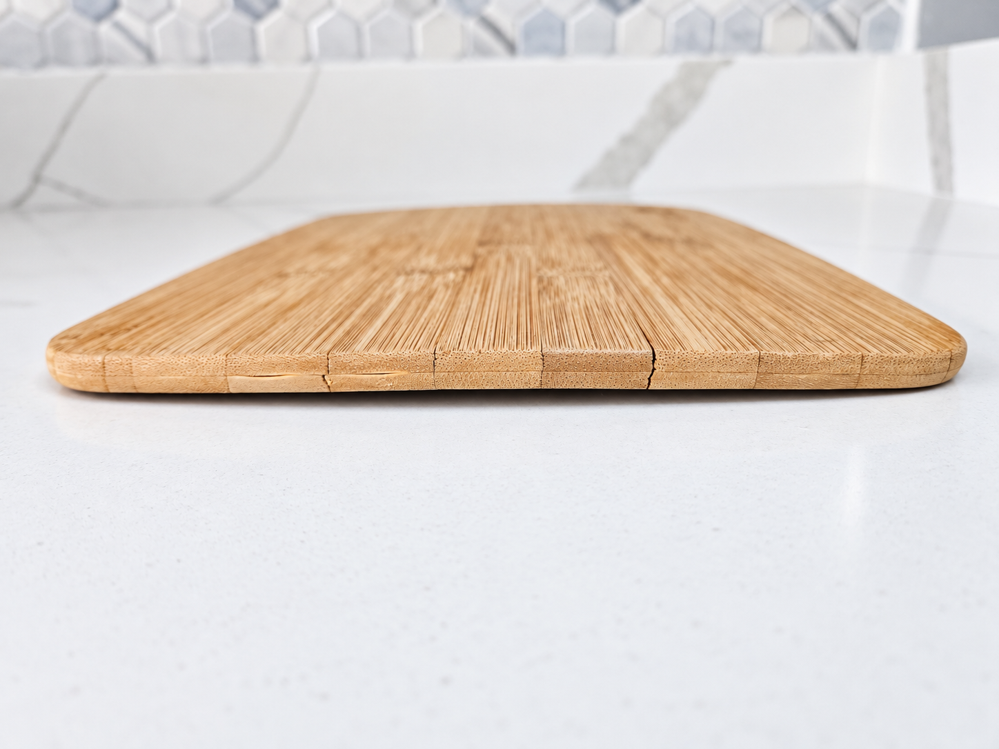 side view of a cracked bamboo cutting board, sitting on top of white marble countertop