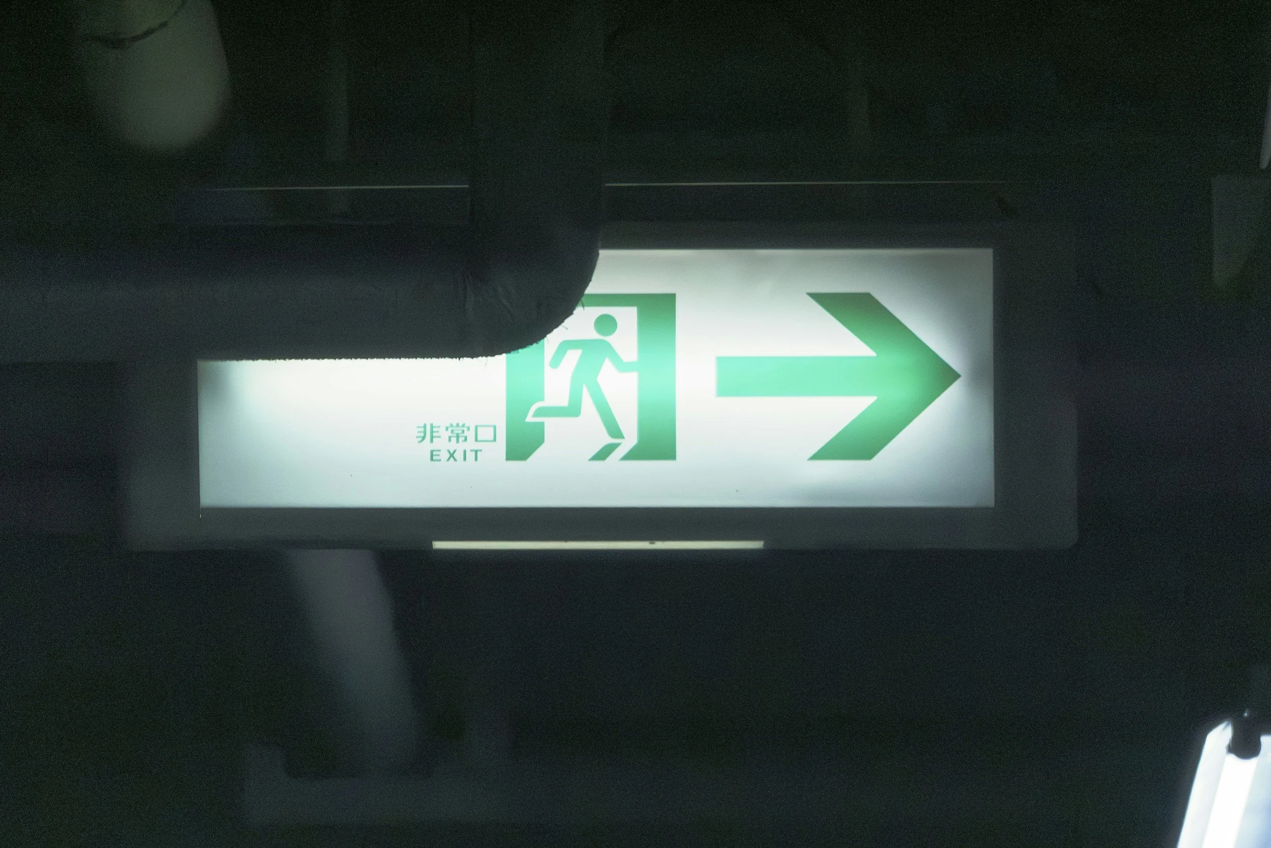Illuminated emergency exit sign with a running figure and an arrow pointing to the right, with Japanese and English text.