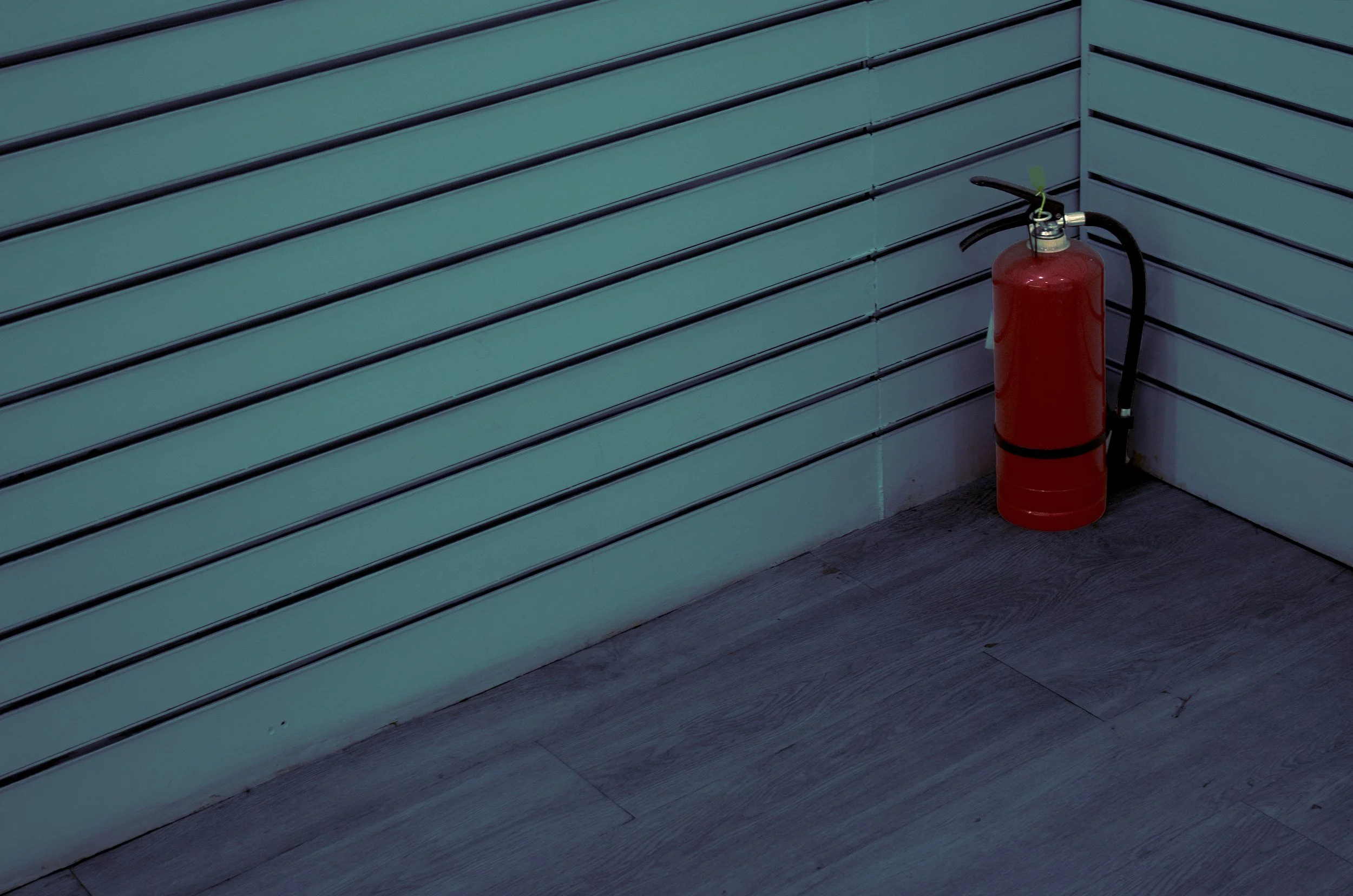 A red fire extinguisher placed on the floor next to a white wall with horizontal black lines.