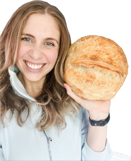 A smiling woman holding a large round loaf of bread.
