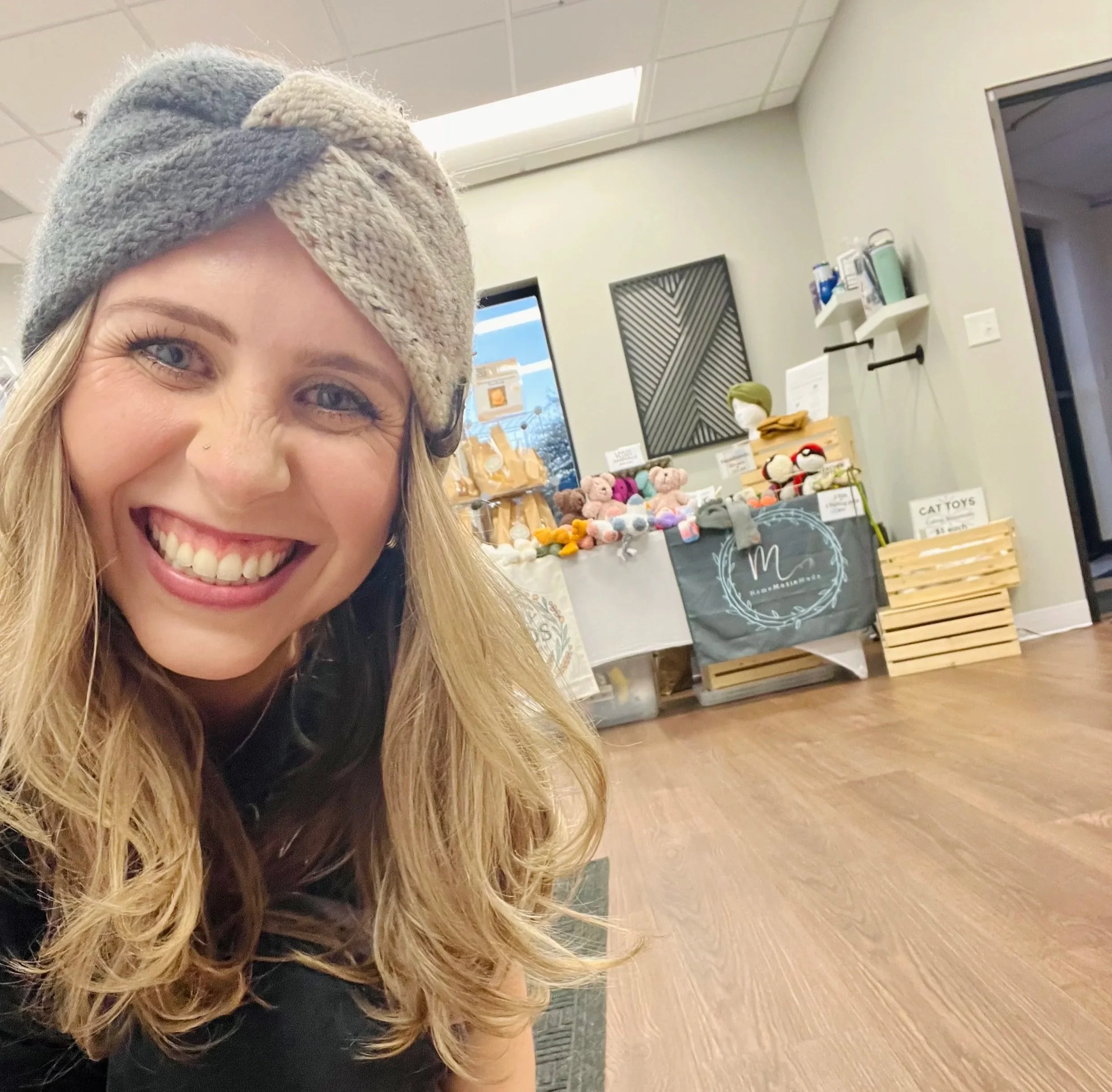 A woman wearing a gray hat and smiling in a store with toys and decorative items displayed on tables and shelves.