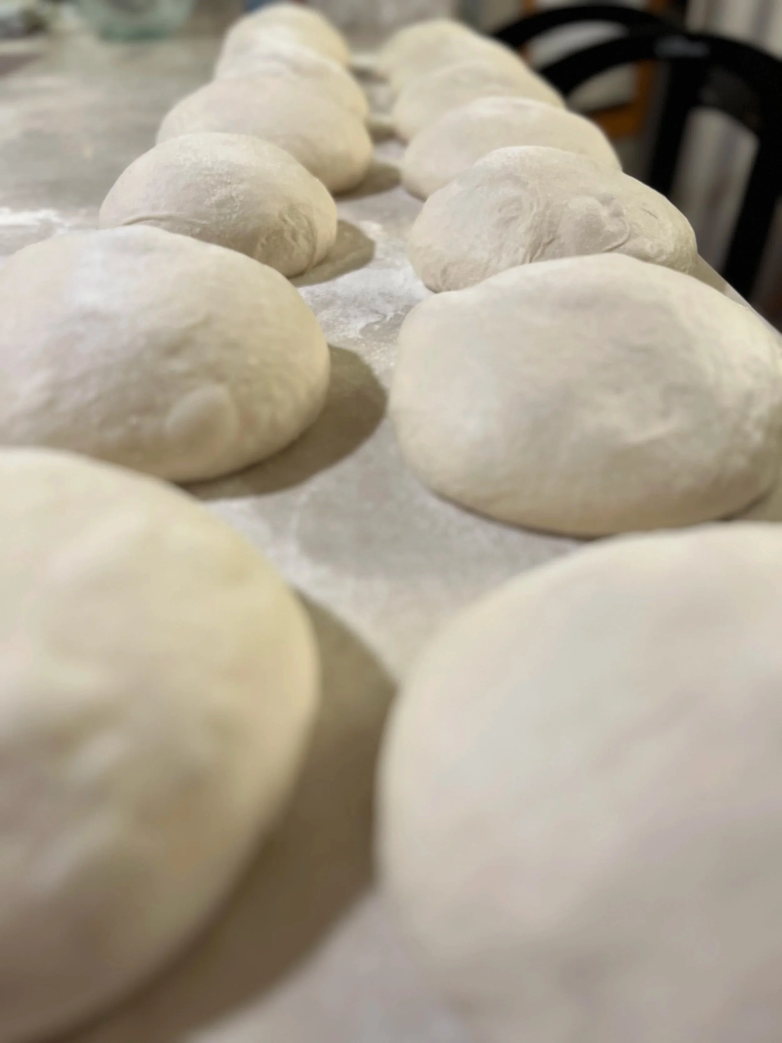 Close-up of round dough balls lined up on a floured surface, ready for baking or frying.