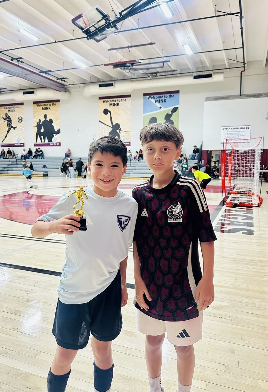 Two young boys standing on a gymnasium court, holding a trophy, celebrating a sports achievement.