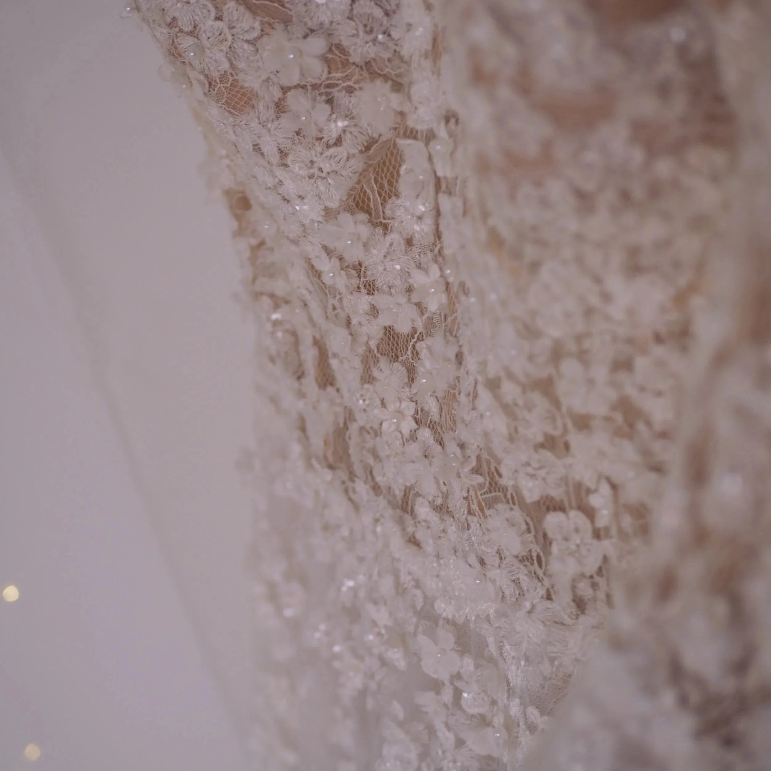 Close-up of beige lace fabric with intricate floral pattern and small, shiny beads or sequins sewn into the lace.