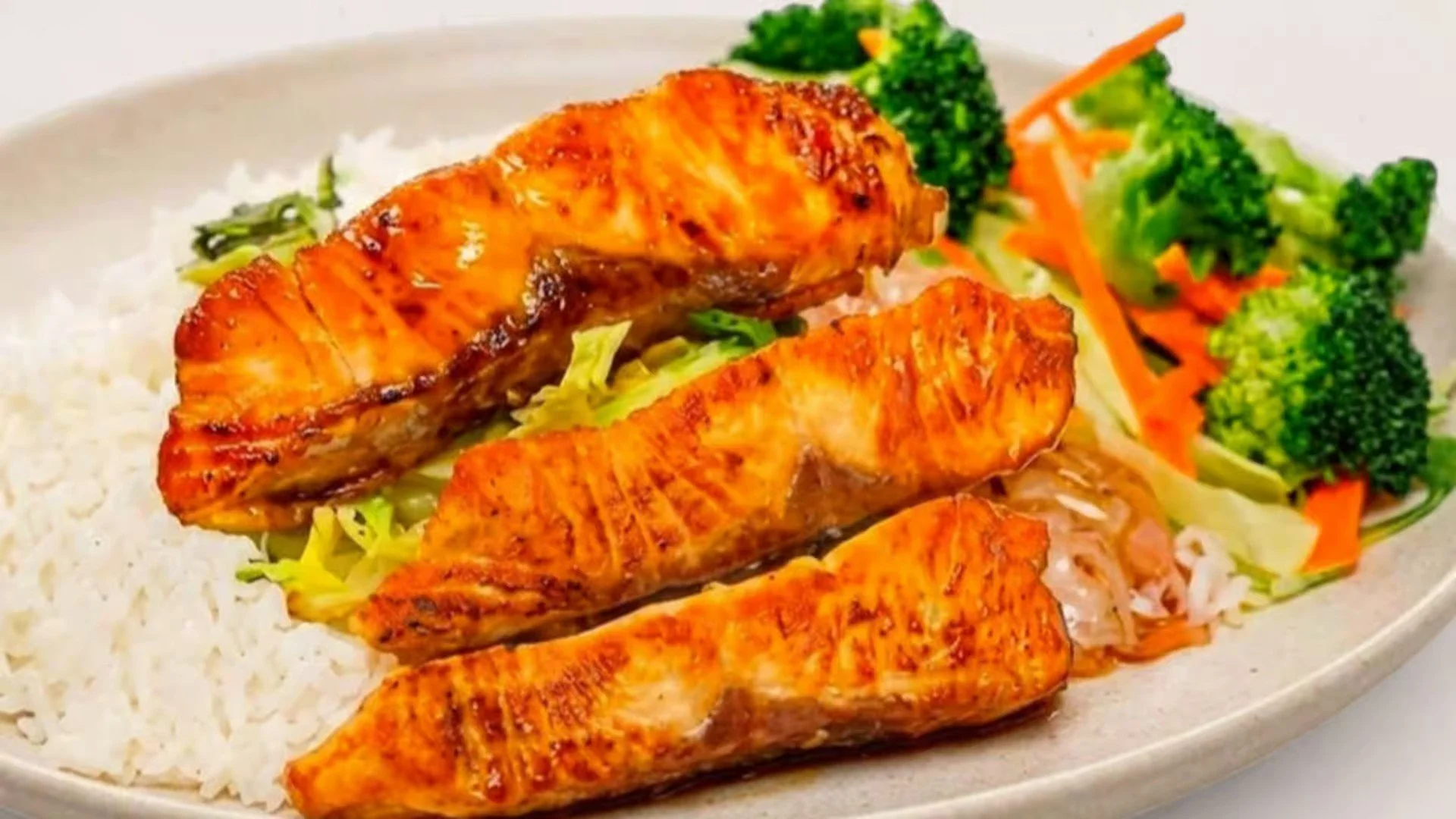 Grilled salmon served with white rice, broccoli, and shredded carrots.