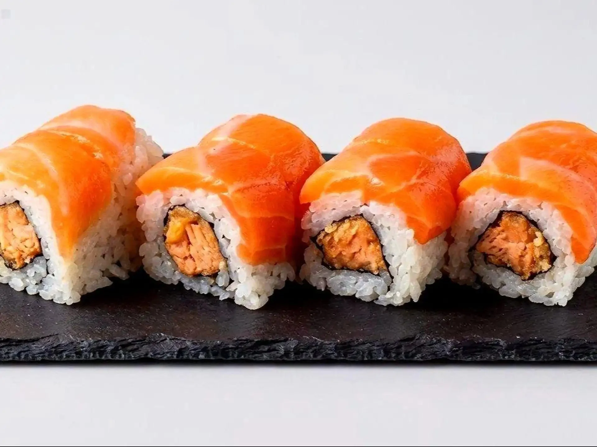 Sushi rolls topped with sliced salmon, arranged on a black slate serving board.