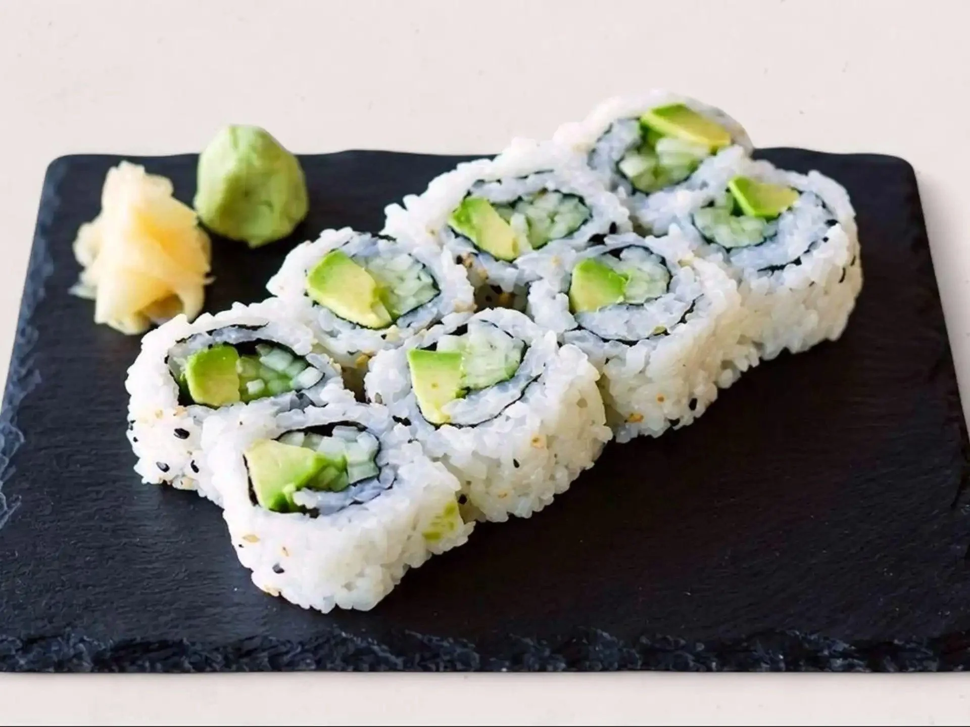 Sushi roll with cucumber inside, served on a black plate with wasabi and pickled ginger