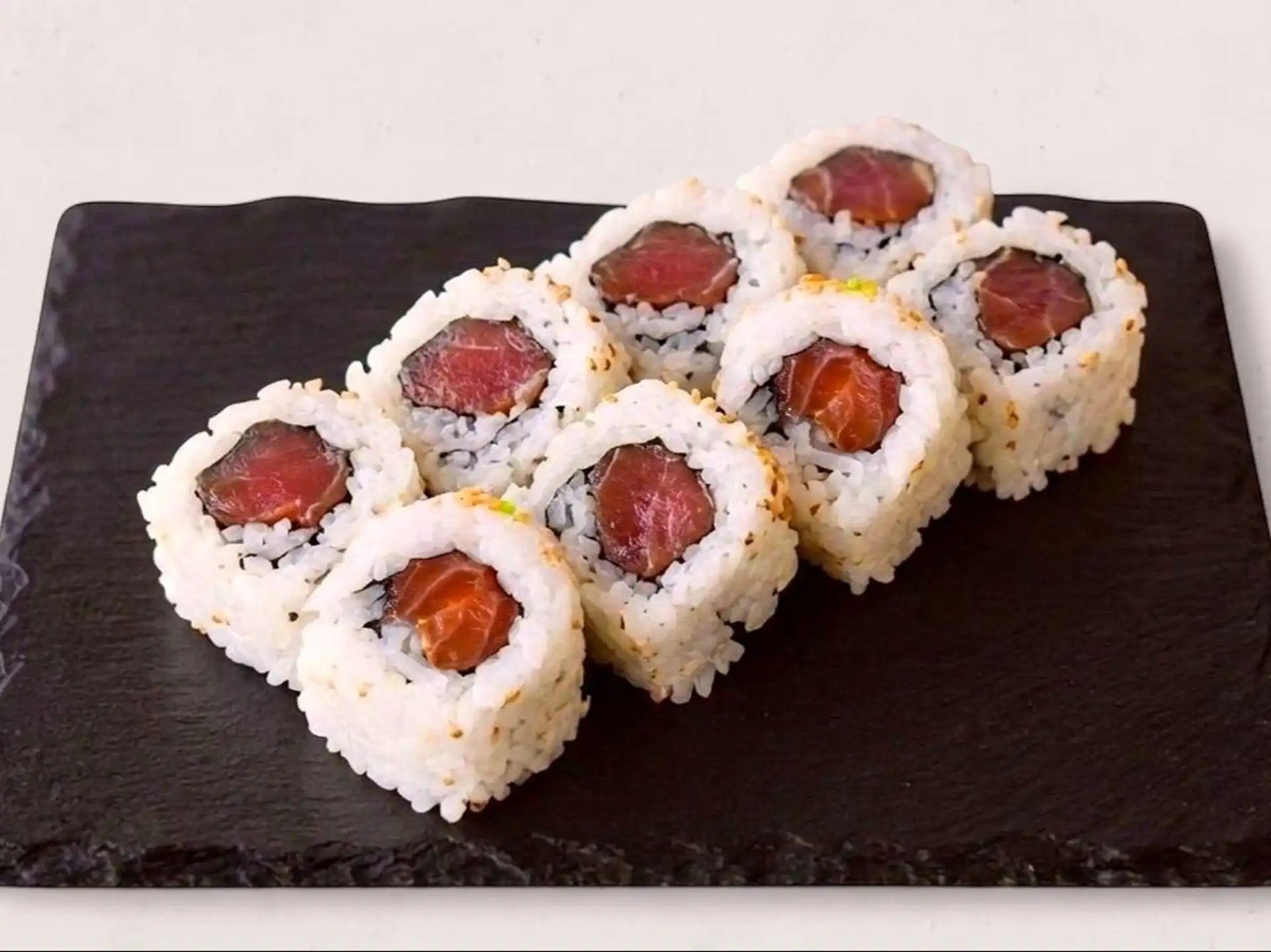 Close-up of six pieces of sushi with raw fish and rice on a dark rectangular platter.