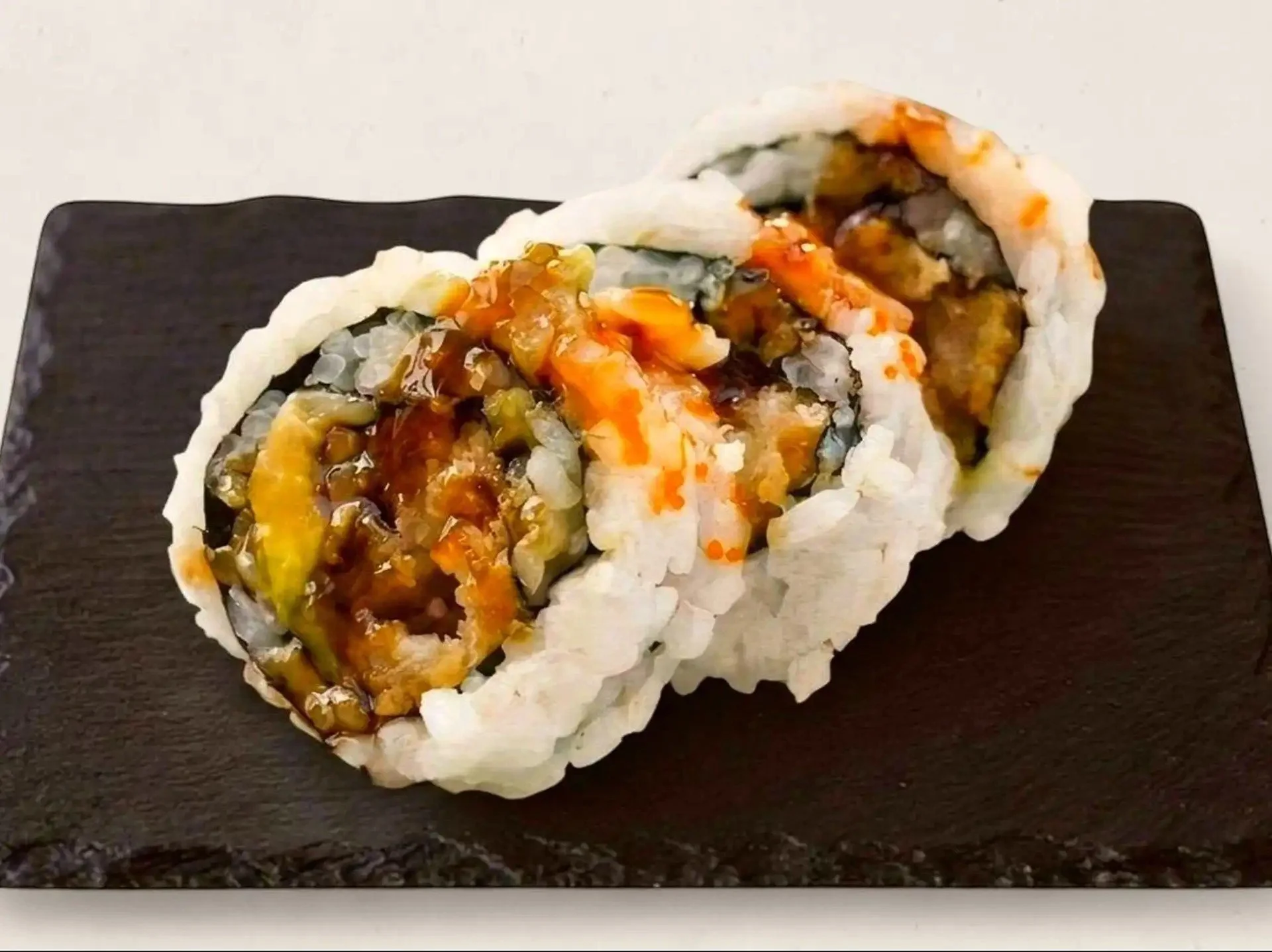 Close-up of a sushi roll with rice, vegetables, and sauce, placed on a black rectangular plate.