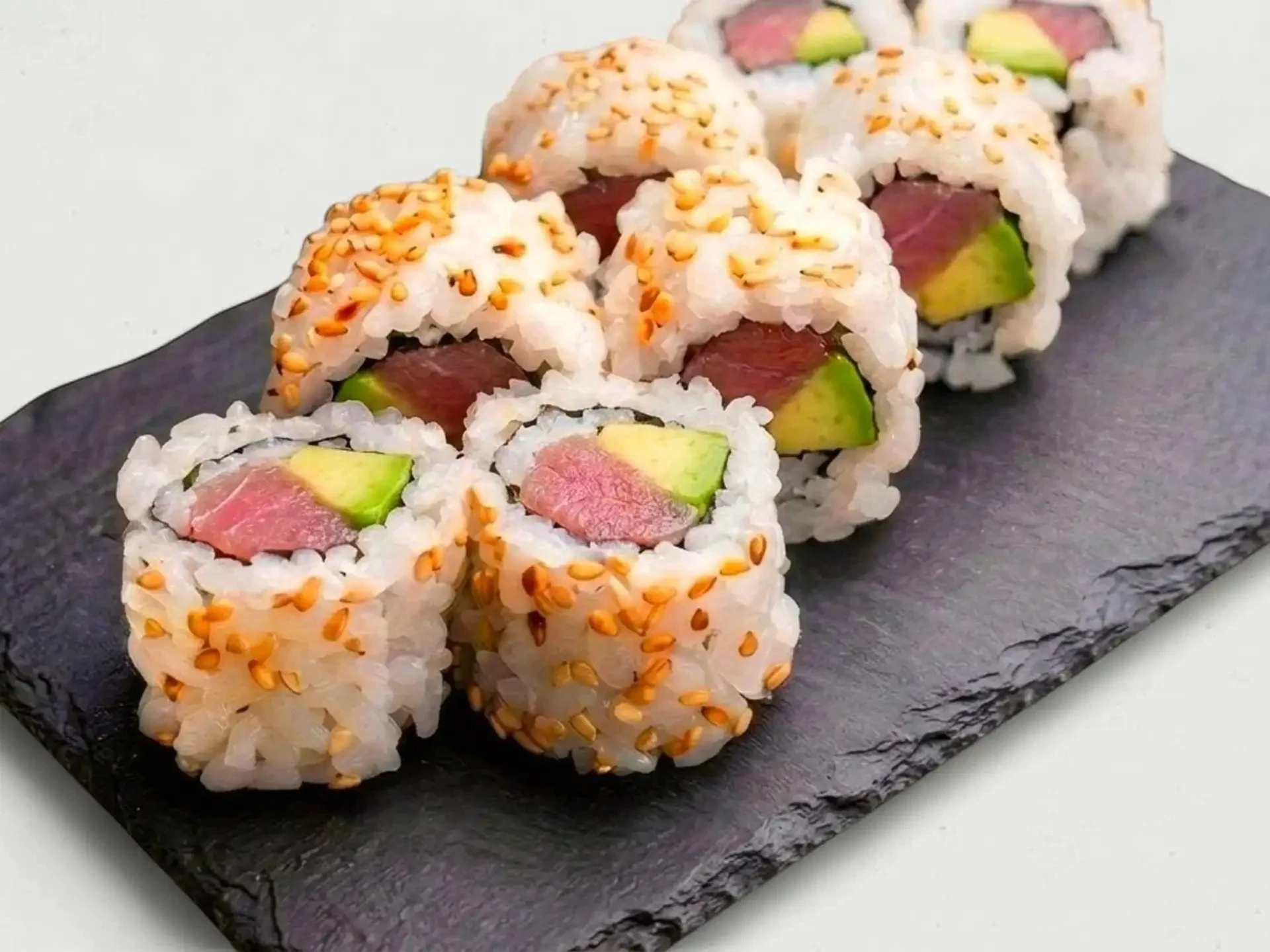 Sushi rolls with raw fish, avocado, and sesame seeds on a black slate serving platter