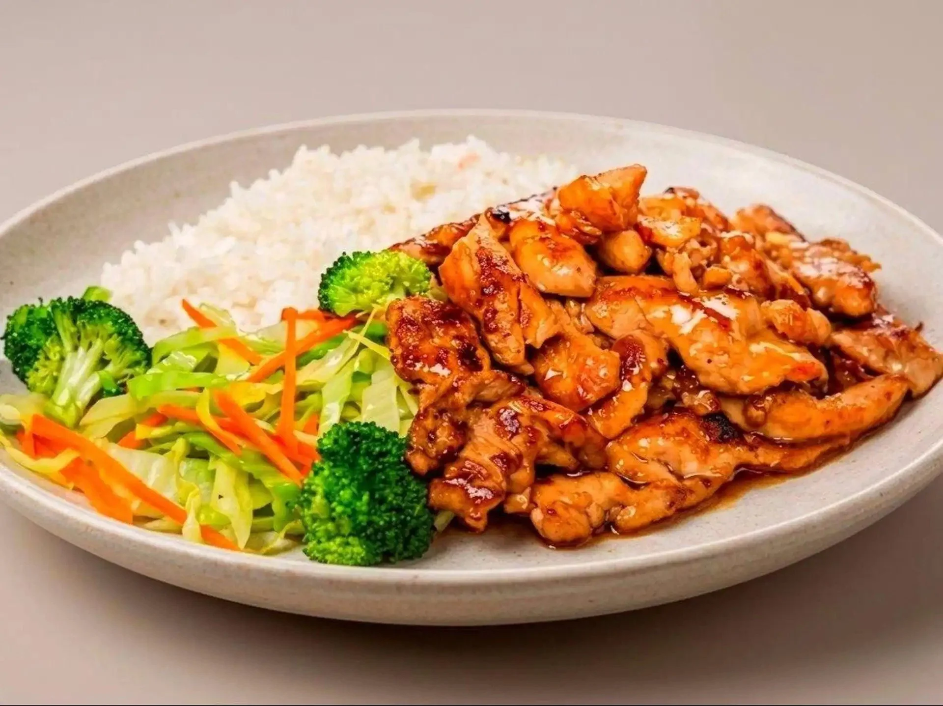 Plate of food with white rice, grilled chicken coated in sauce, steamed broccoli, shredded carrots, and mixed salad greens.