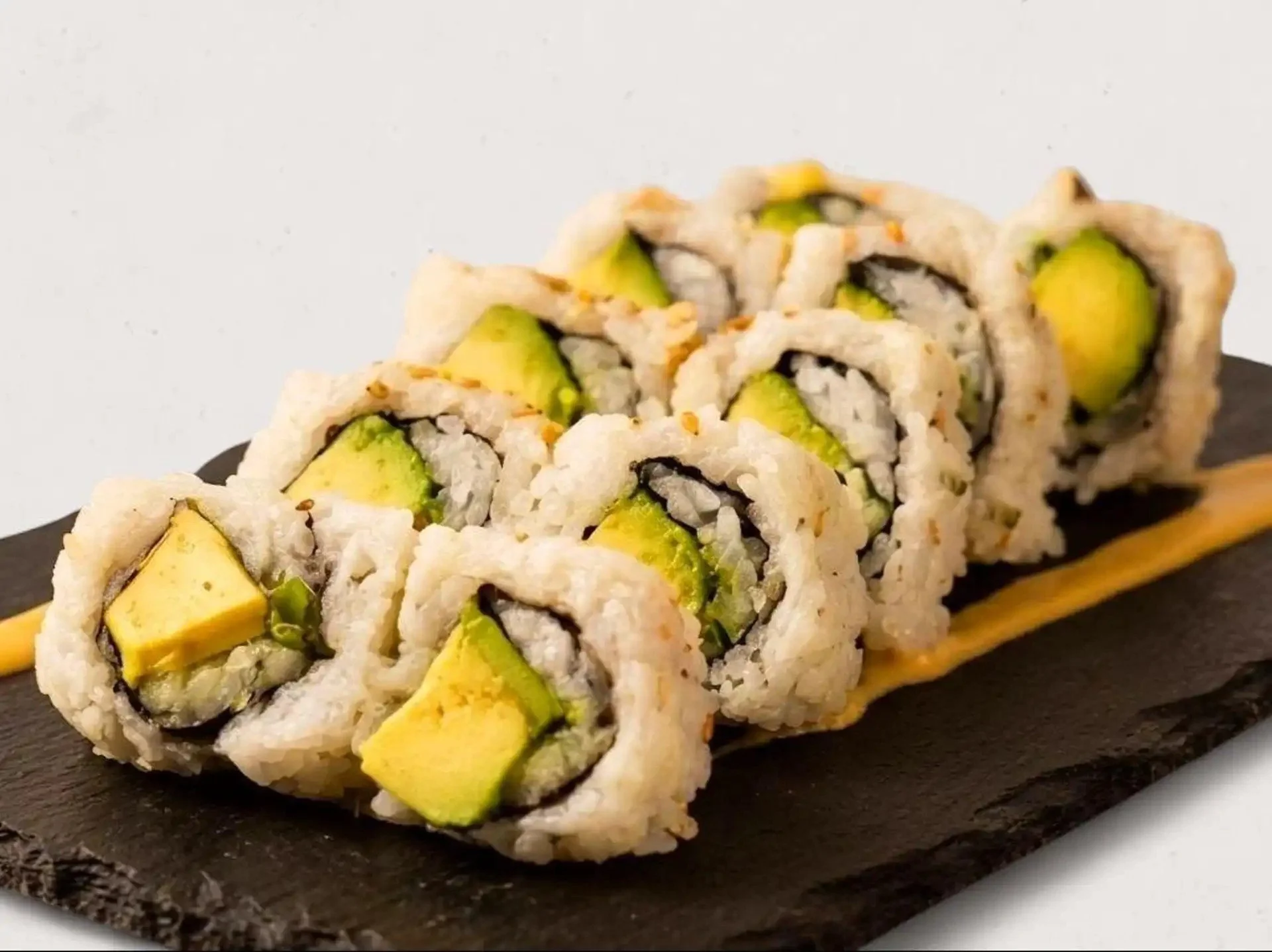 Close-up of sushi rolls with avocado and rice, served on a black slate plate.