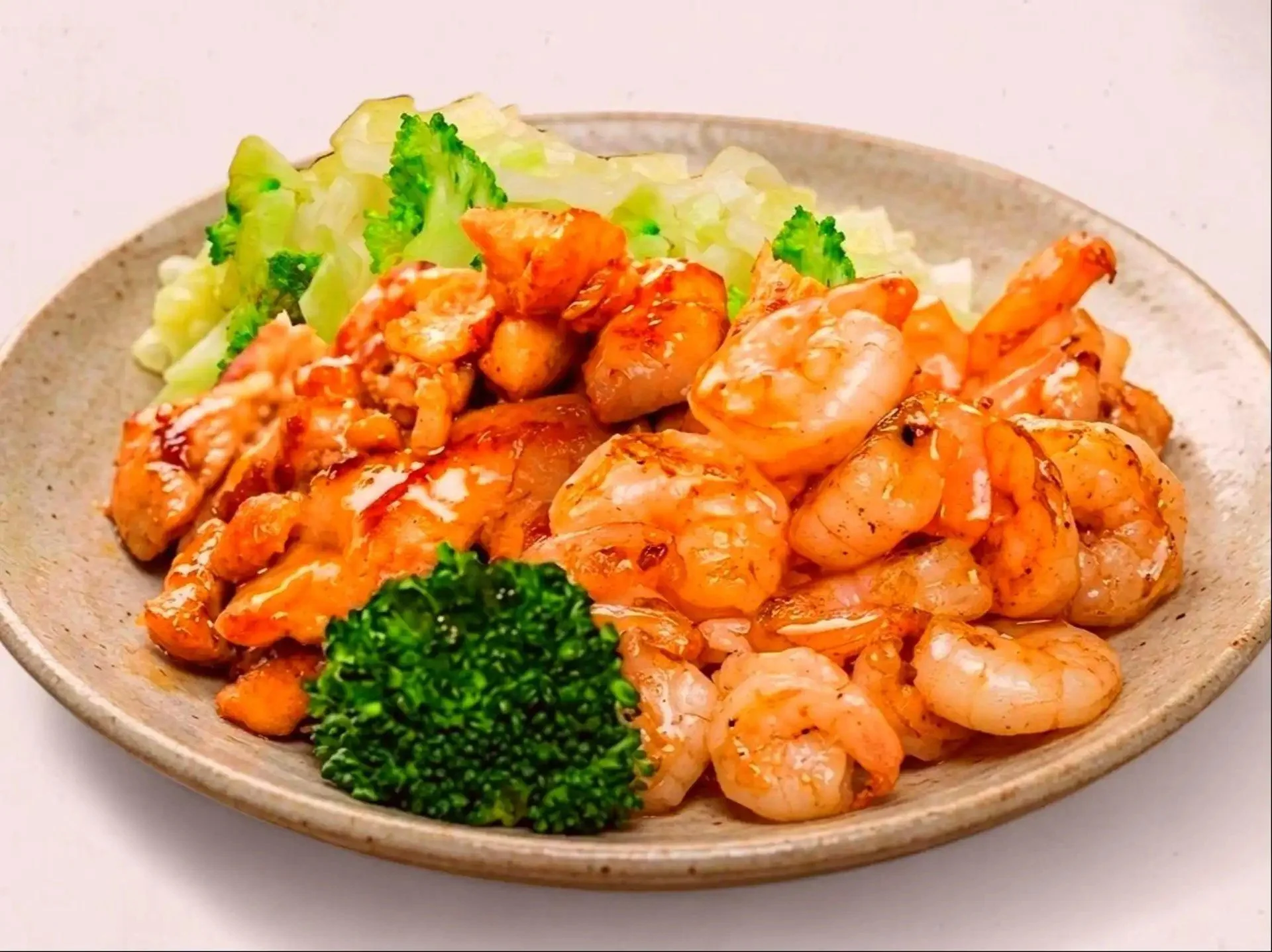 A beige ceramic plate with cooked shrimp, grilled chicken chunks, steamed broccoli, and shredded lettuce.