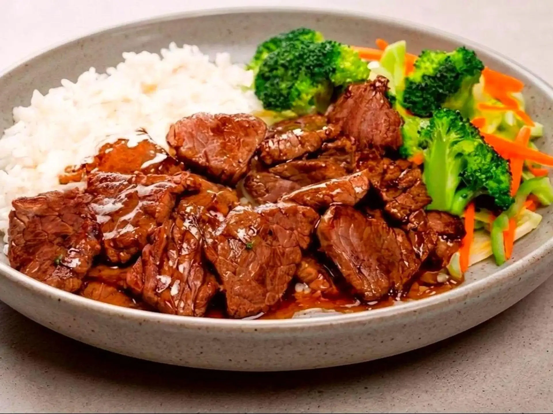 A plate of cooked white rice, beef stew with gravy, and steamed broccoli and carrots.