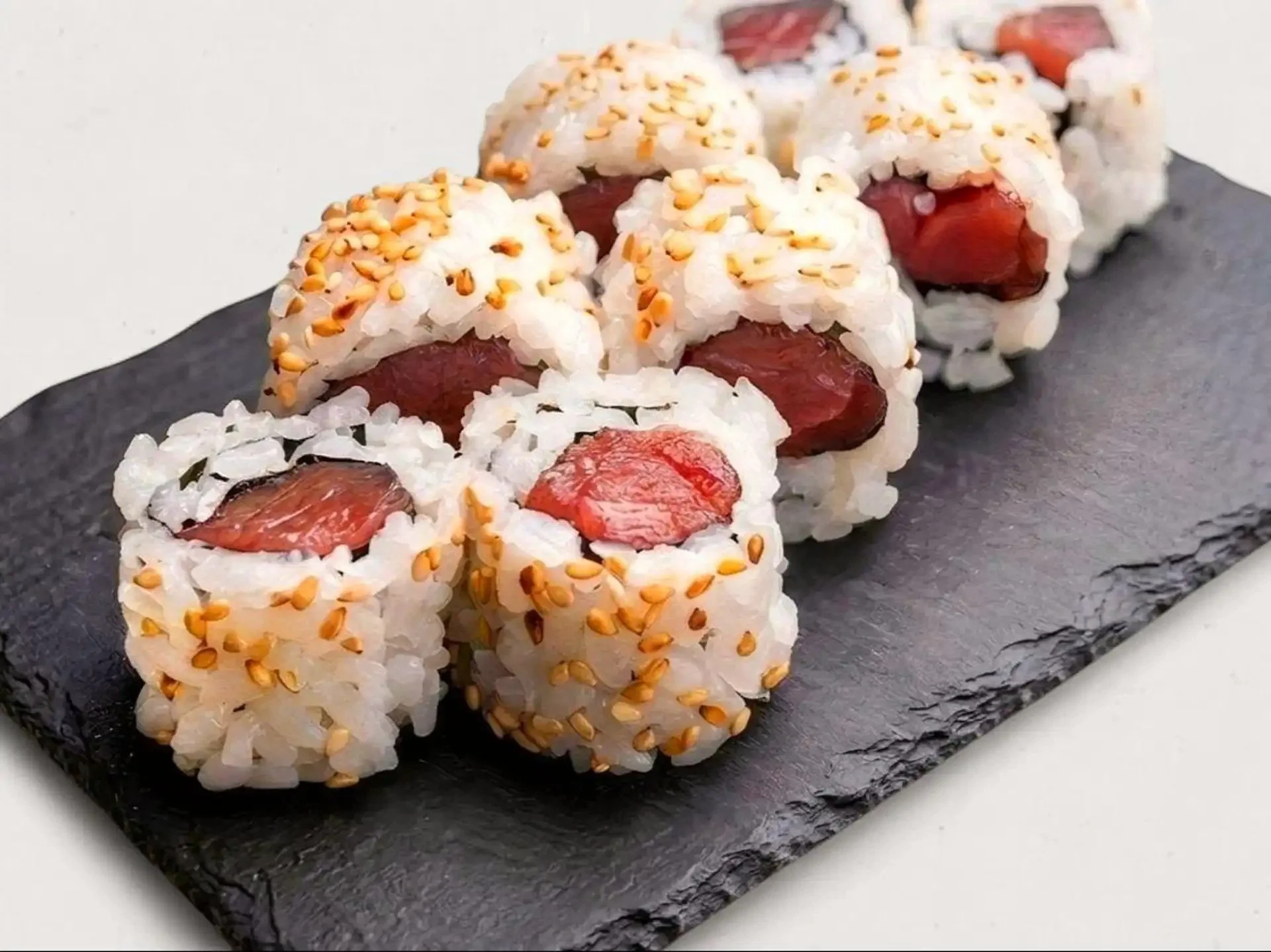 Close-up of sushi rolls with rice, raw fish, sesame seeds, on a black slate serving tray