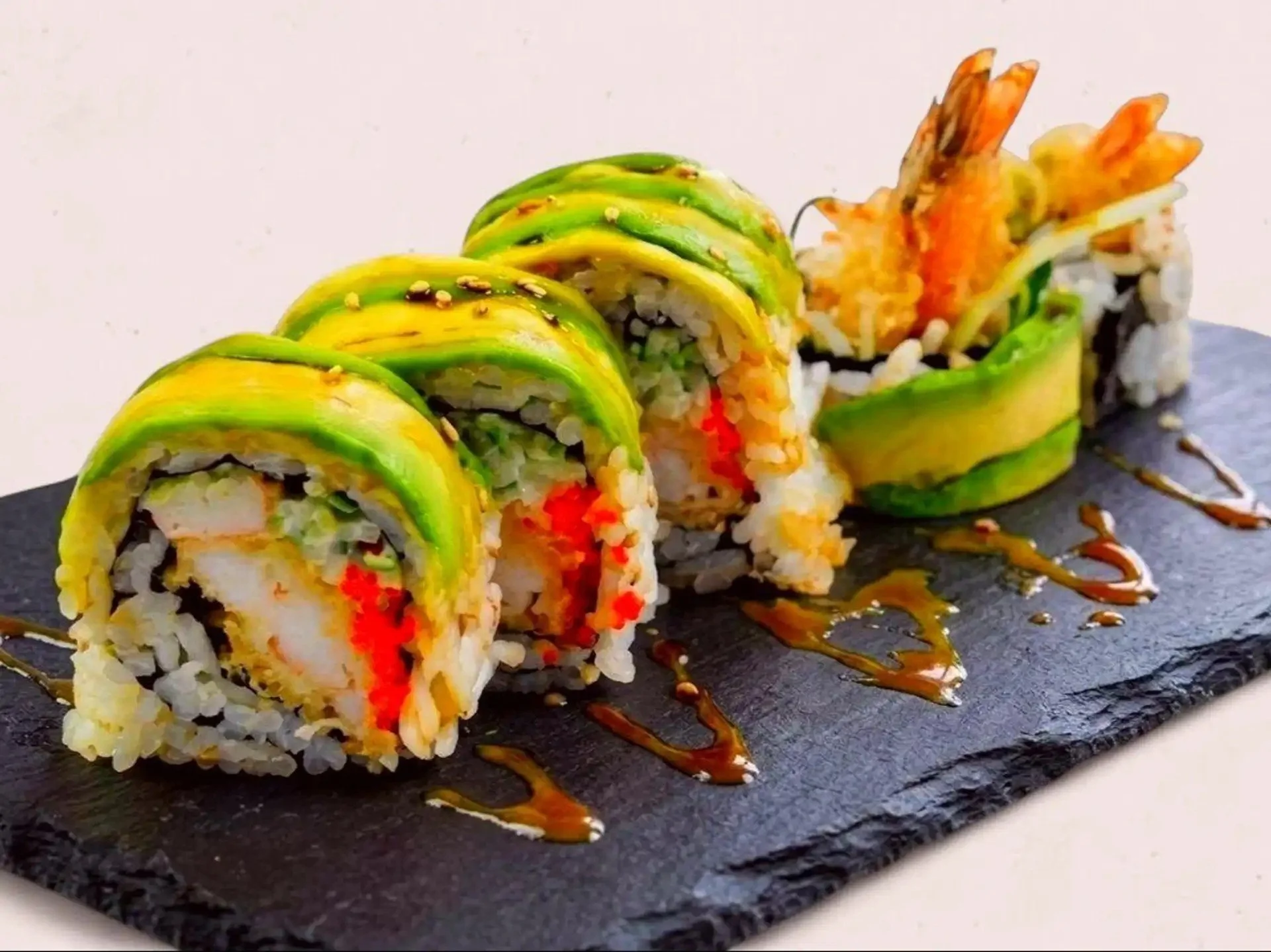Close-up of sushi rolls with eel sauce on a black slate plate.