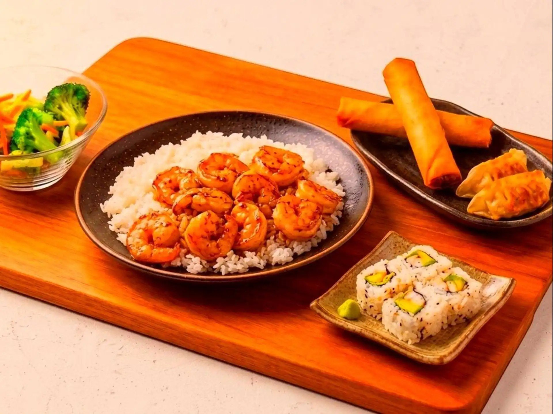 Assorted Japanese sushi and sashimi platter with rolled sushi, shrimp, and vegetables, served on a wooden board.