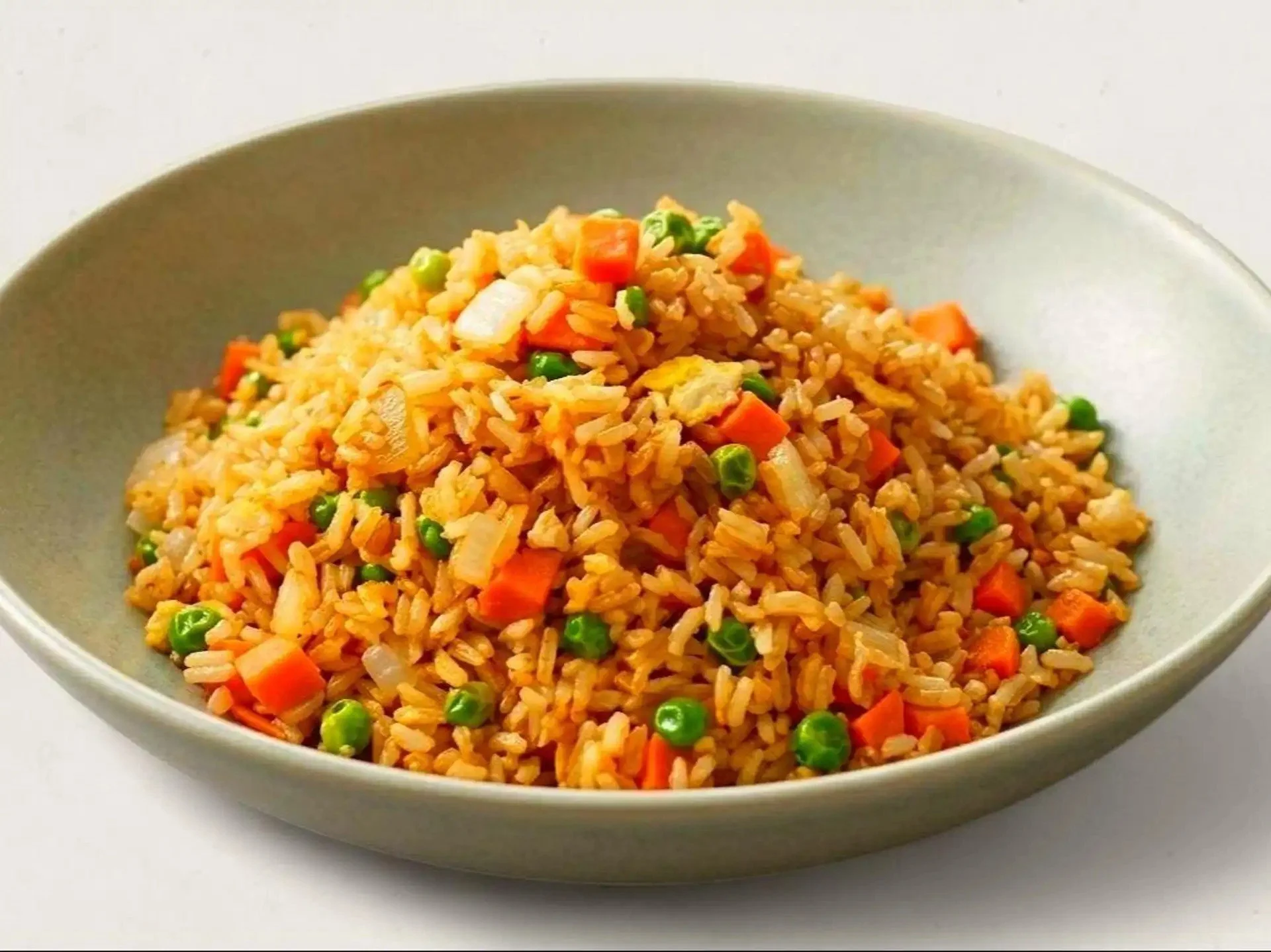 A bowl of cooked fried rice with vegetables, including peas, carrots, and chopped onions.