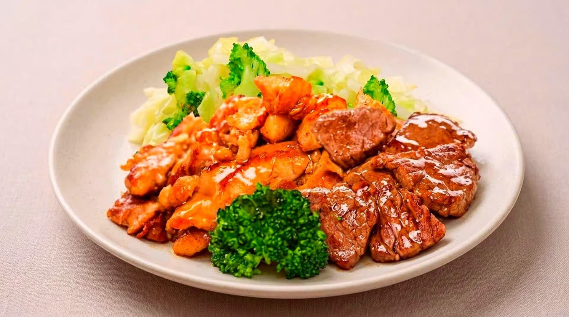 A plate of cooked meat topped with sauce, along with broccoli, diced potatoes, and a small serving of cooked cabbage.