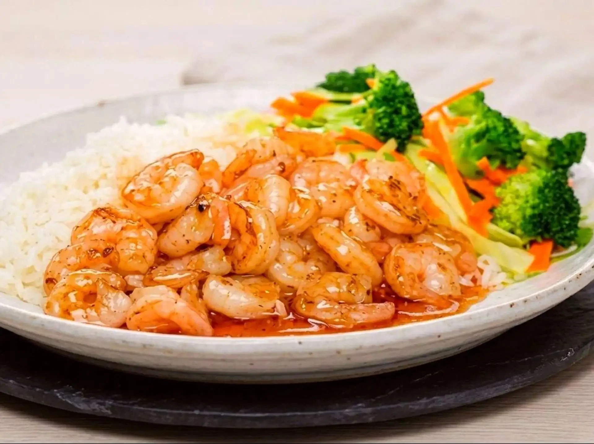 Plate of cooked shrimp, steamed broccoli, shredded carrots, and white rice.