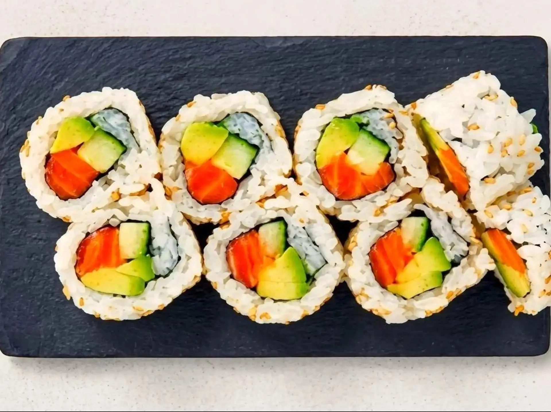 Sushi rolls filled with cucumber, avocado, and carrot, arranged in a row on a dark rectangular plate.