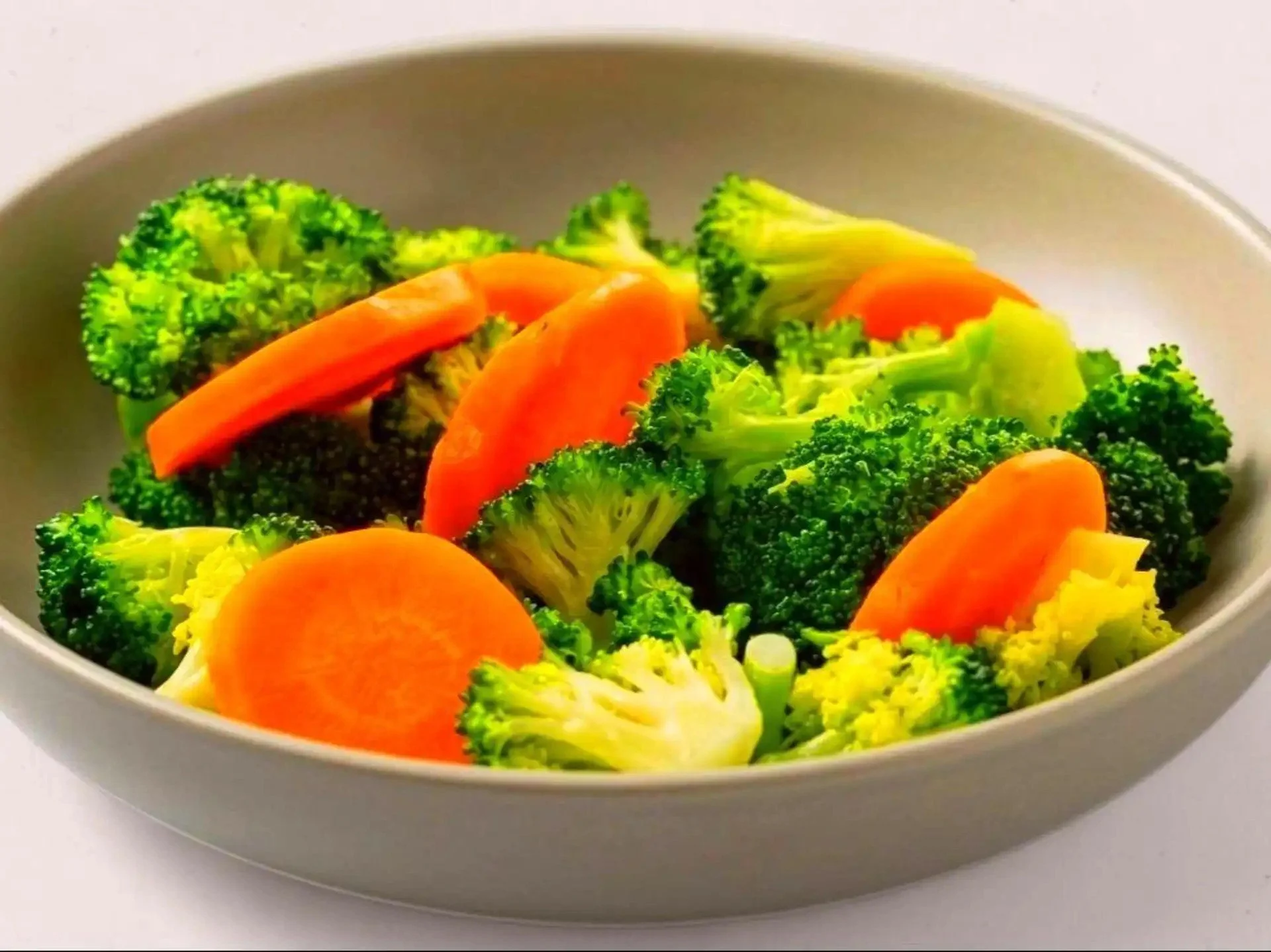 A white bowl filled with steamed broccoli florets and sliced carrots.