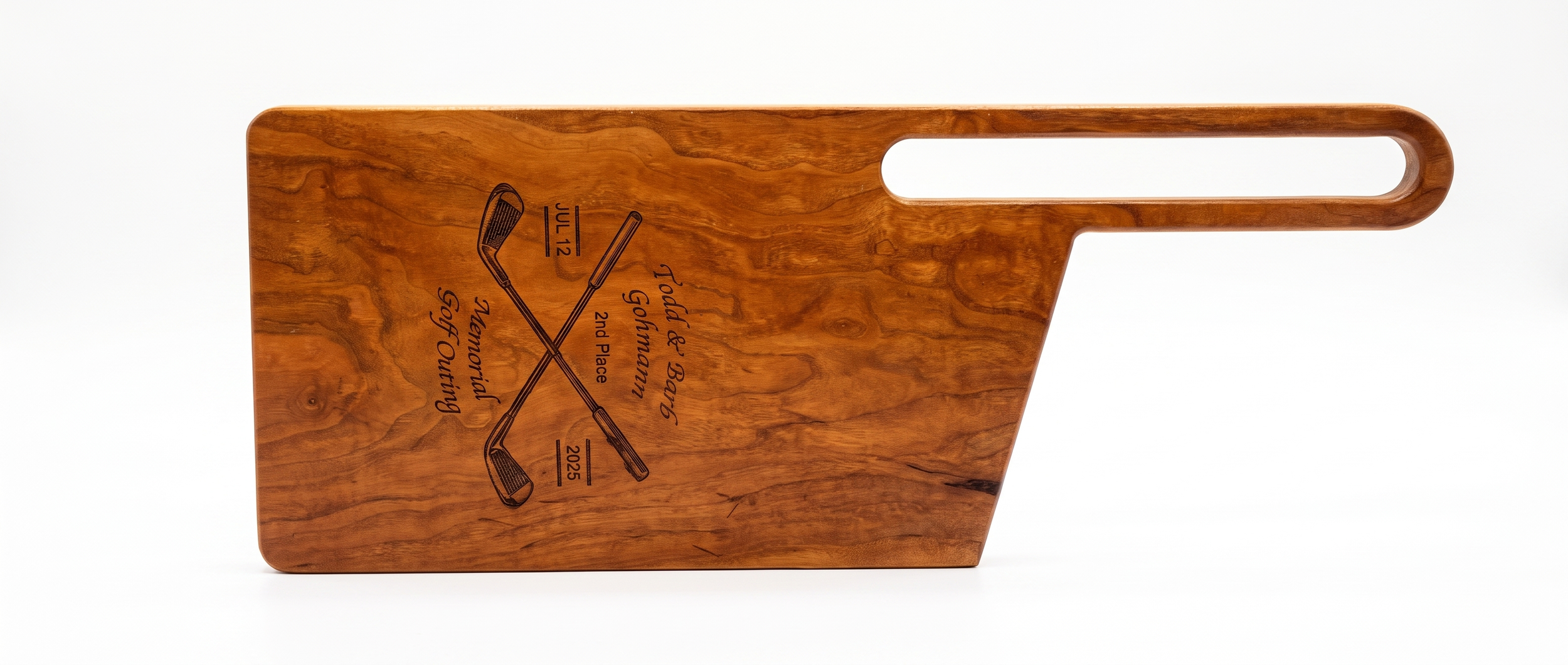 A wooden cutting board with engraved golf-themed text and illustrations, including crossed golf clubs. The engraving mentions Todd & Bugg Gahmann, Memorial Golf Outing, July 12, 2025, Second Place.