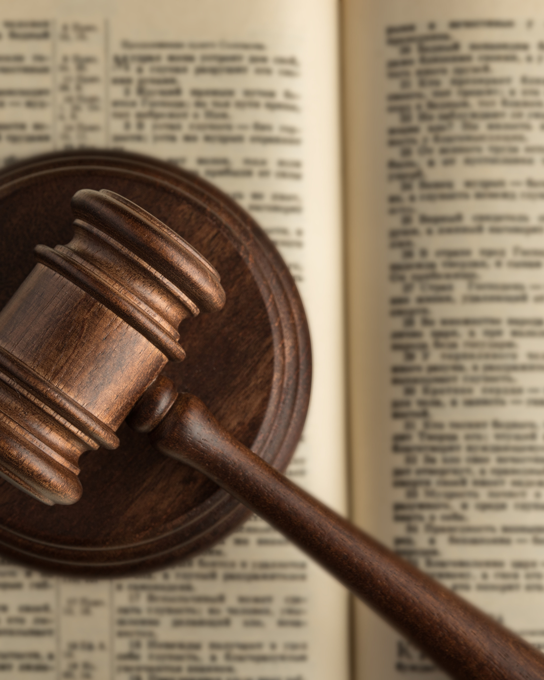 A wooden gavel resting on a sound block, placed on an open book with densely packed text.