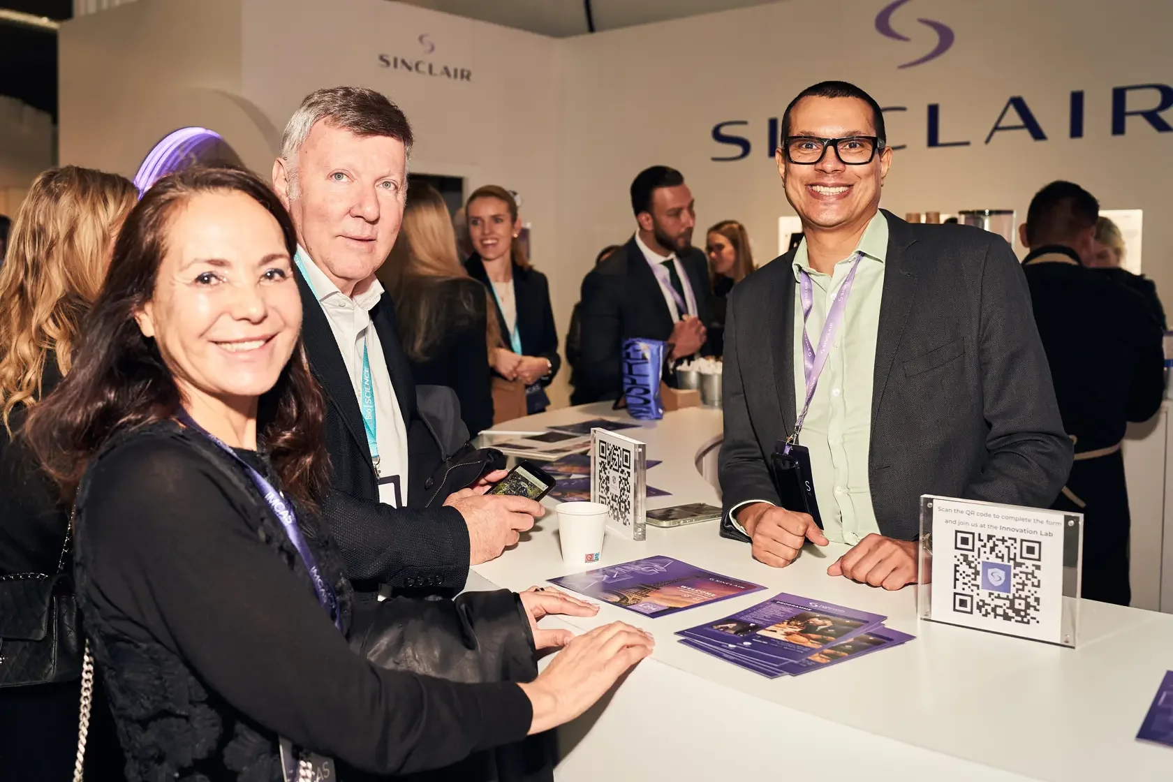 Group of professionals at a conference booth with company branding, QR codes, and informational materials on the table.