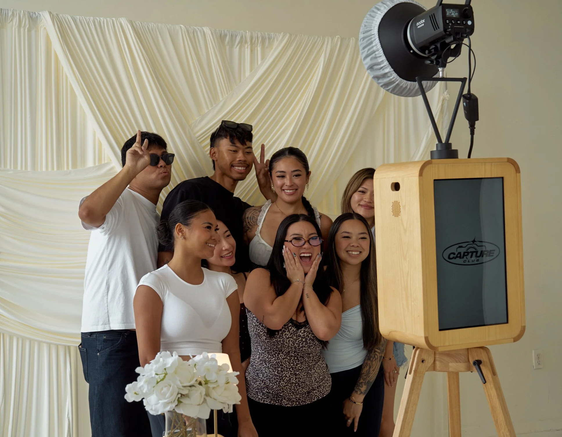 A group of diverse people gathered together, smiling for a photo in front of a vintage photo booth at a celebration event.
