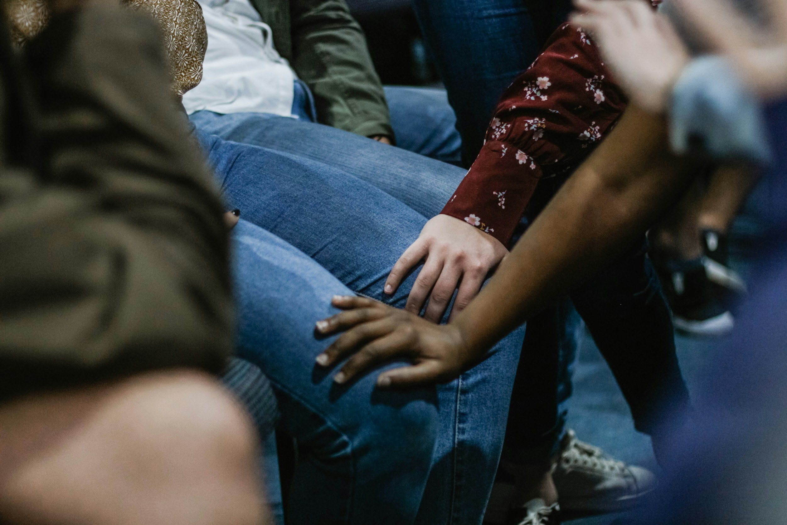 People sitting close together, holding hands on their laps, in a group setting.