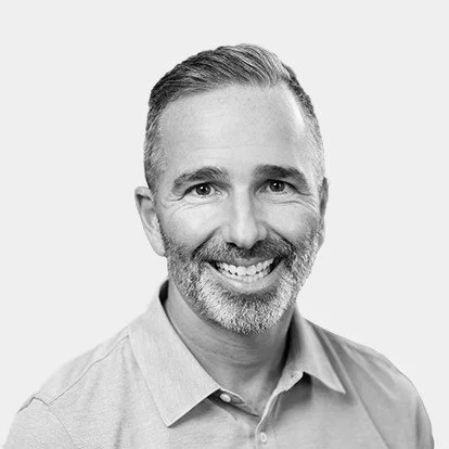 Black and white portrait of a smiling man with short hair and a beard, wearing a collared shirt.
