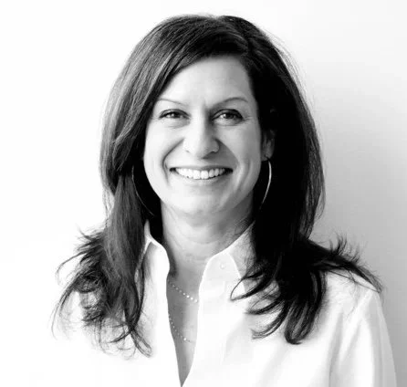 A smiling woman with shoulder-length hair and hoop earrings, wearing a collared shirt.