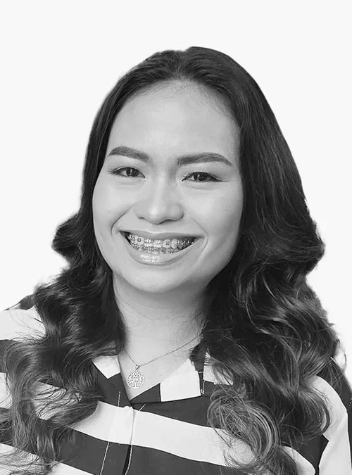 Black and white portrait of a smiling woman with long, wavy hair and braces, wearing a striped top and a necklace.