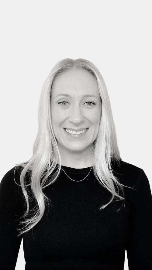 A woman with long blonde hair smiling in front of a white background.