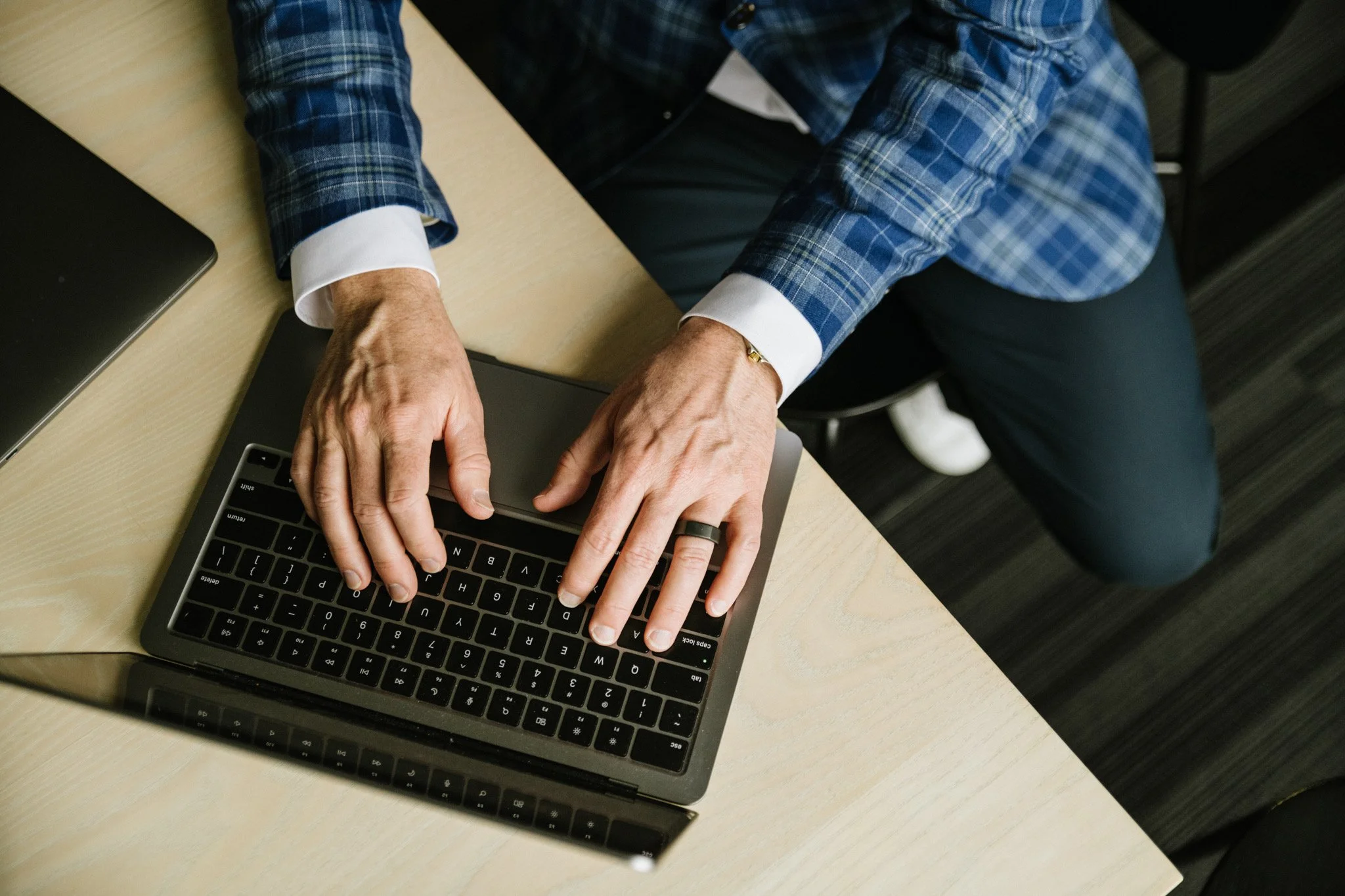 A person wearing a blue plaid jacket and white shirt working on a laptop at a desk.
