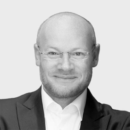 Black and white portrait of a bald man wearing glasses and a suit, smiling at the camera.