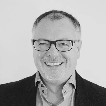 Black and white headshot of a smiling man with glasses, short hair, and a collared shirt.