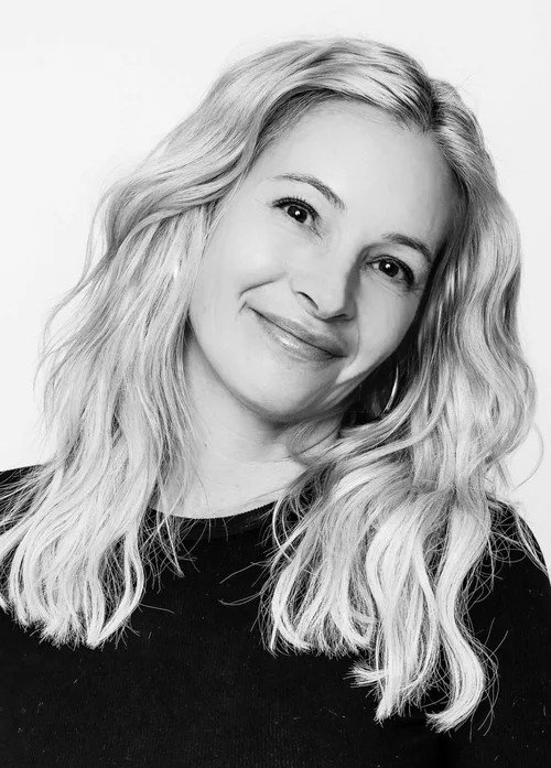 Black-and-white portrait of a woman with long, wavy blonde hair smiling softly.