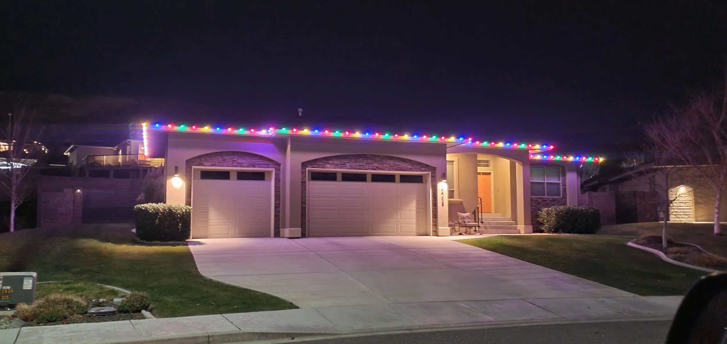 A suburban house at night decorated with colorful Christmas lights along the eaves.