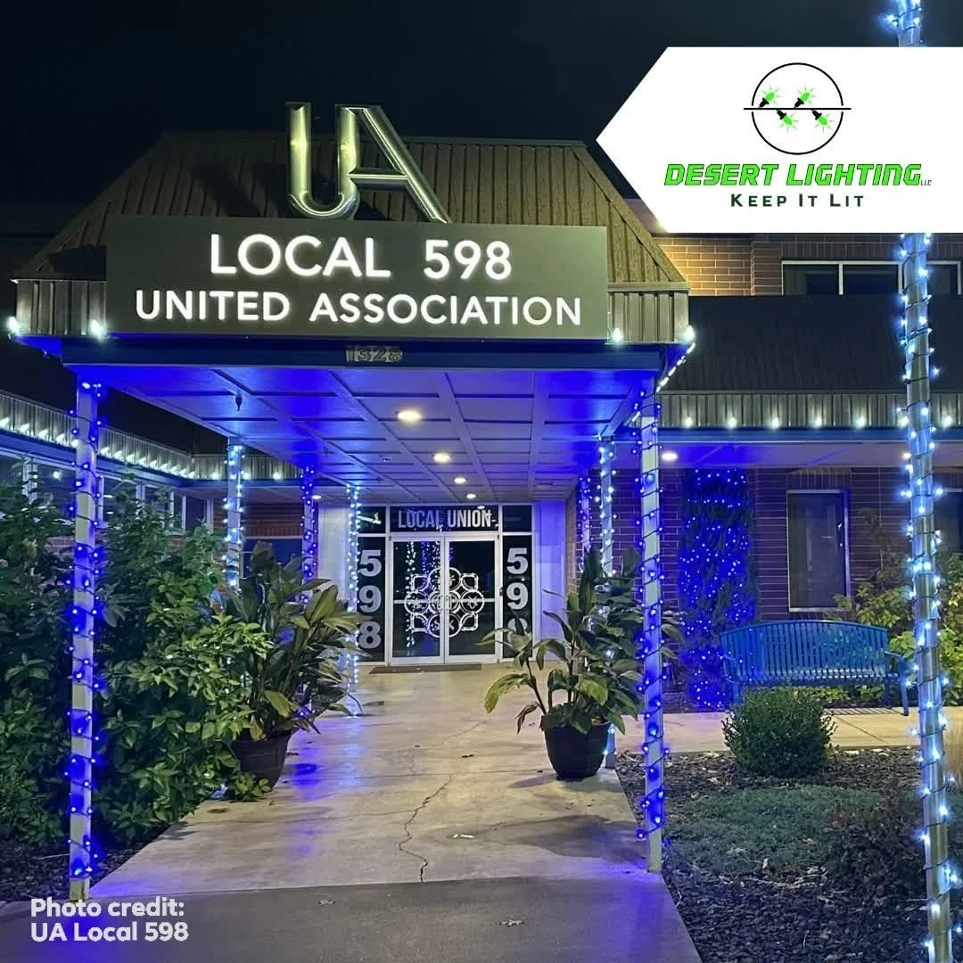 Entrance to a building decorated with blue and white string lights, plants in pots, and a bench. Signs indicate involvement with UA Local 598 and United Association.