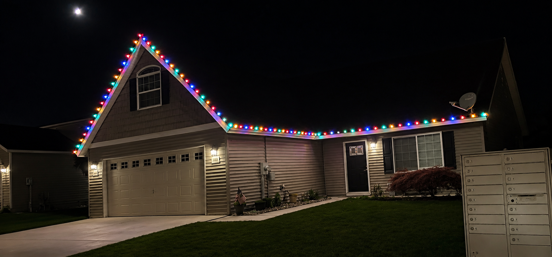 A house decorated with colorful Christmas lights along the roofline at night, with a bright moon in the sky.