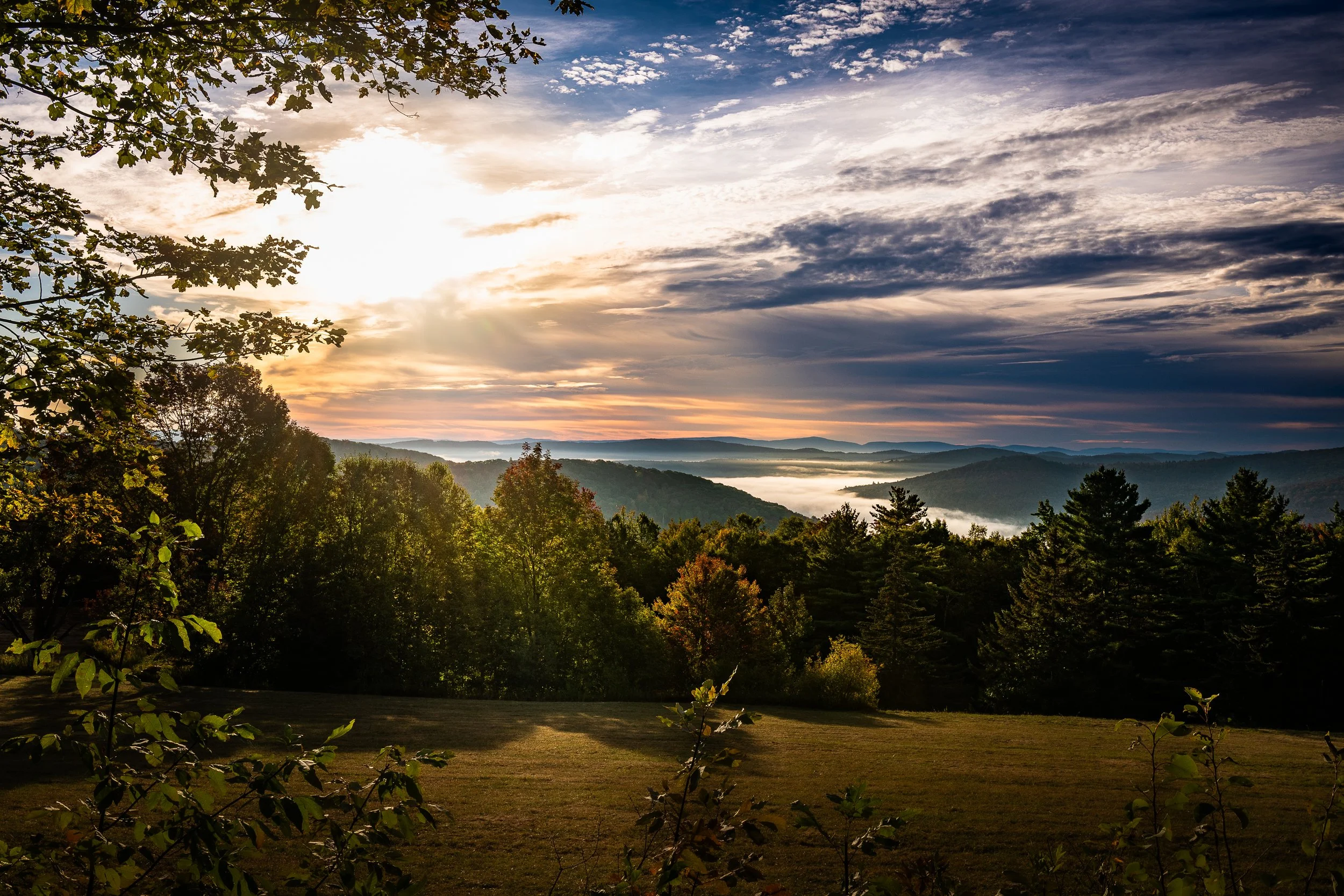Sunrise over a valley with a river, surrounded by trees and mountains.