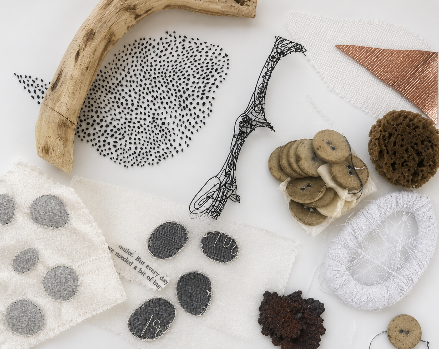 Assorted eco-friendly and recycled materials, including a piece of driftwood, fabric swatches, buttons, wire, mesh, sponge, and other textured objects on a white background.
