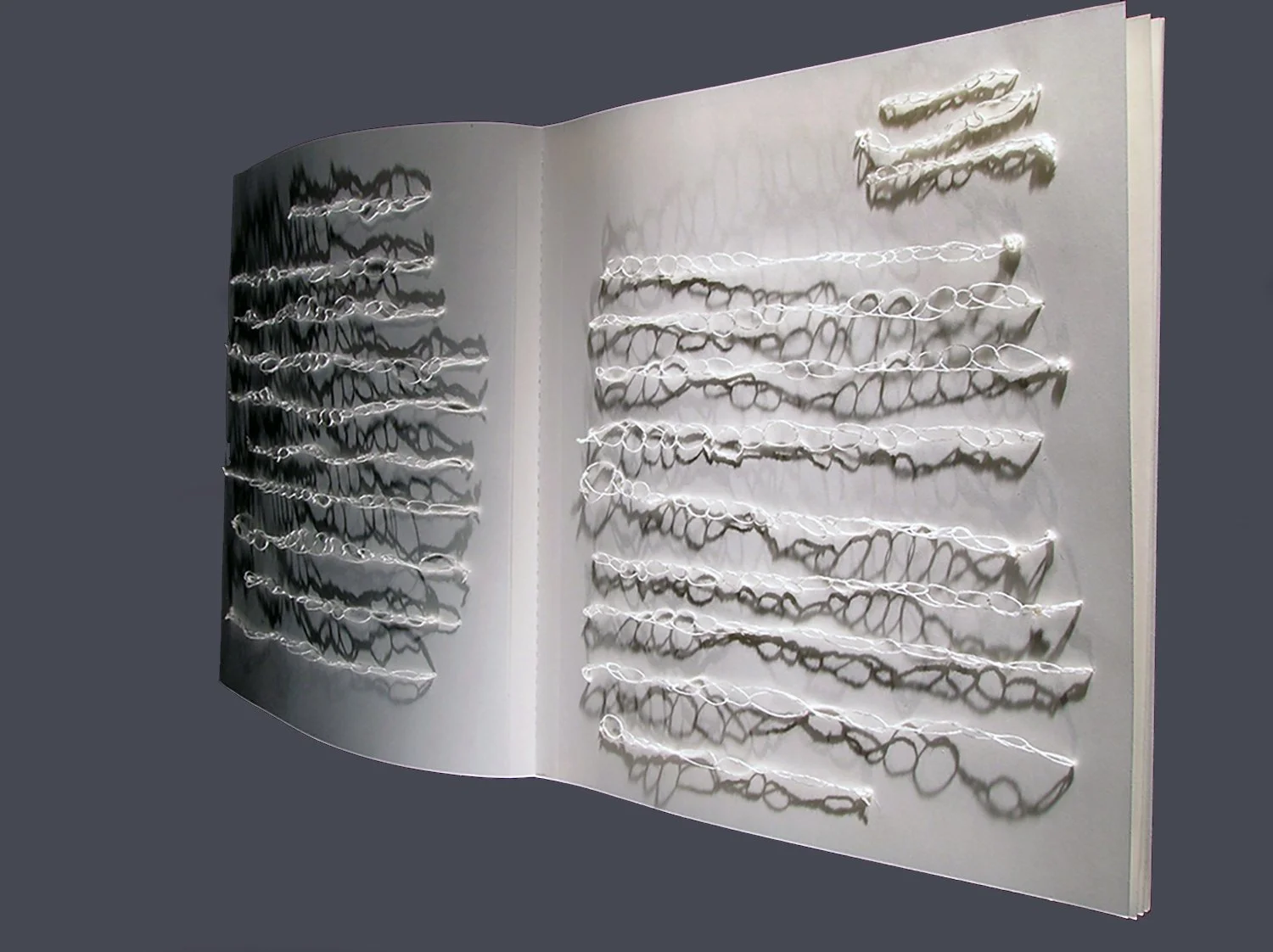 Open book with white strings attached to pages, creating intricate shadow patterns.