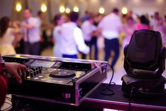 DJ equipment with a DJ mixing console and a moving head light in front of a dance floor with people dancing at a party.