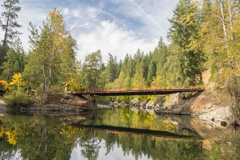 Bridge over a calm river surrounded by trees with fall foliage.