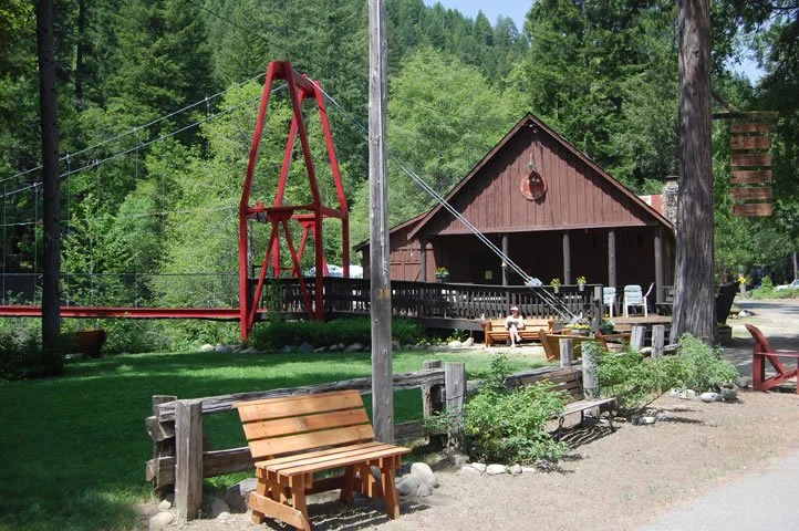 Outdoor scene with wooden benches, a wooden building, and a red swing set in a green, forested area.